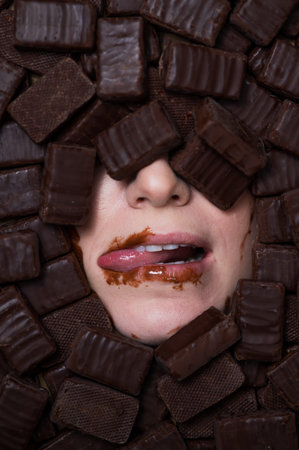 The face of a caucasian woman surrounded by sweets. Girl licks chocolate-stained lips