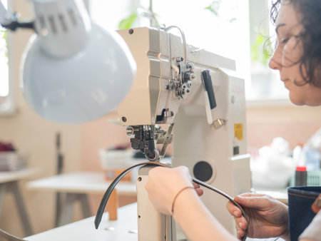 A woman tanner sews a leather belt on a sewing machineの写真素材