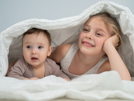 Little girl and her newborn brother hiding under the blanketの写真素材