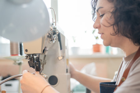 A woman tanner sews a leather belt on a sewing machineの写真素材
