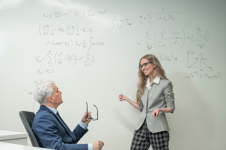 Female student answers a question from an elderly professor at a white boardの写真素材