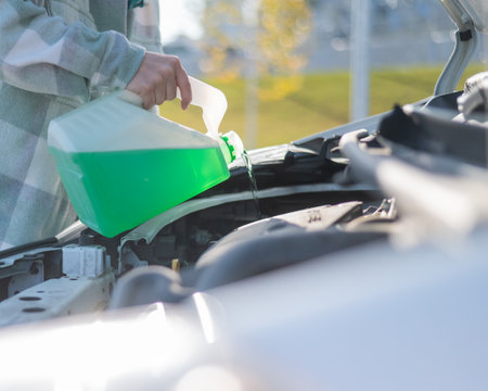 Close up of female hands filling car reservoir with windshield washer fluid from bottleの写真素材