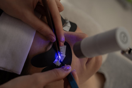 A woman undergoing eyelash extension procedure using an ultraviolet lamp