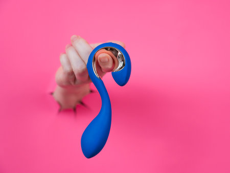 Hand with blue object sticking out through pink paper backgroundの写真素材