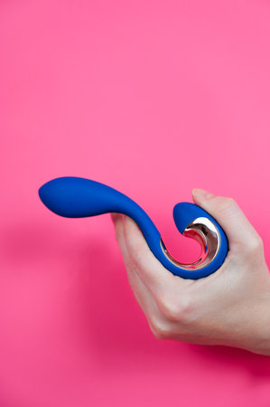 Hand with blue object sticking out through pink paper background. Vertical photoの写真素材