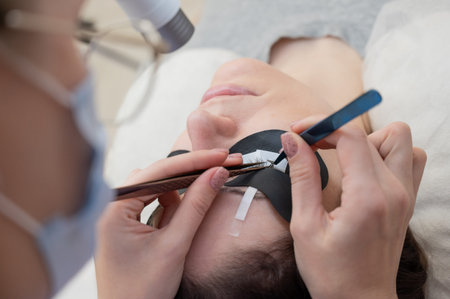 A woman undergoing eyelash extension procedure using an ultraviolet lamp