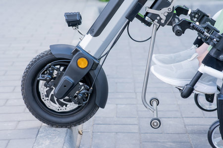 A faceless woman in a wheelchair with an assistive device for manual control. Electric handbike