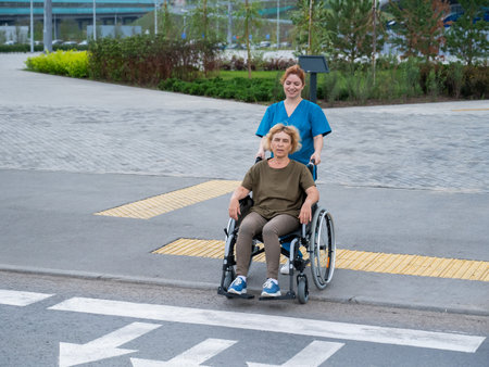 Red-haired nurse pushing an elderly woman in a wheelchair across the roadの写真素材