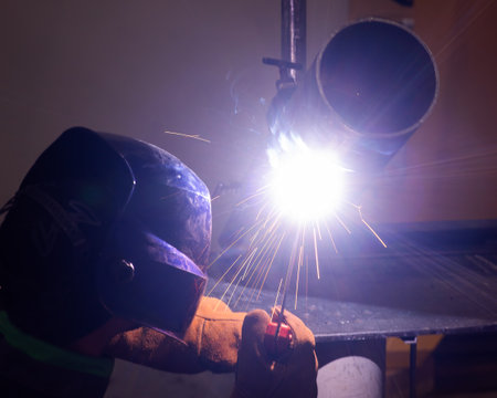 A man wearing a protective mask welds a metal pipeの写真素材