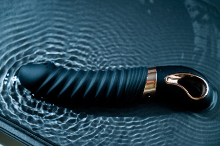 Black silicone vibrator in water. Circles on water around toy