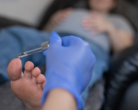 Pregnant woman getting a pedicure in a beauty salon. The technician applies moisturizing oil to the clients feetの写真素材
