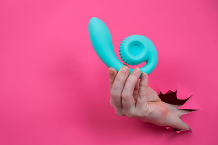 Hand with blue object sticking out through pink paper background. Copy space