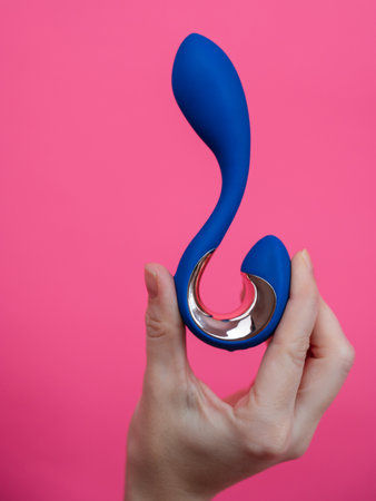 Woman holding blue curved object on pink background. Vertical photoの写真素材