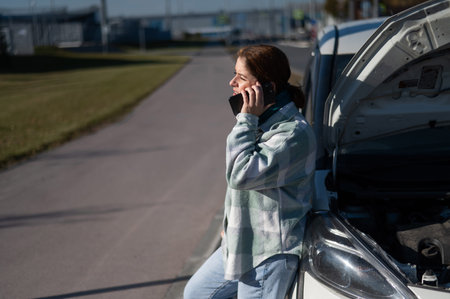 Sad Caucasian woman calling on phone while standing near car with open hood