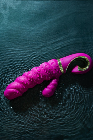 Pink ribbed vibrator in water. Circles on water around toyの写真素材