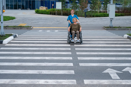 Red-haired nurse pushing an elderly woman in a wheelchair across the roadの写真素材