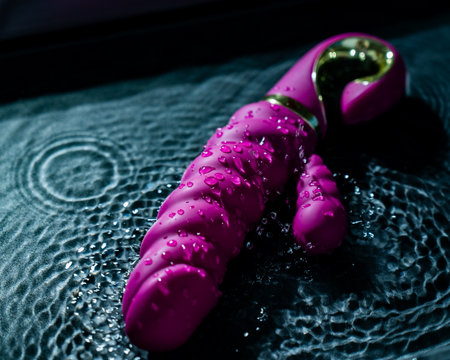 Pink ribbed vibrator in water. Circles on water around toyの写真素材