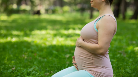 Pregnant caucasian woman doing yoga in the park. Close-up of the abdomen