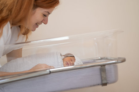A young mother admires her newborn son in the maternity hospital
