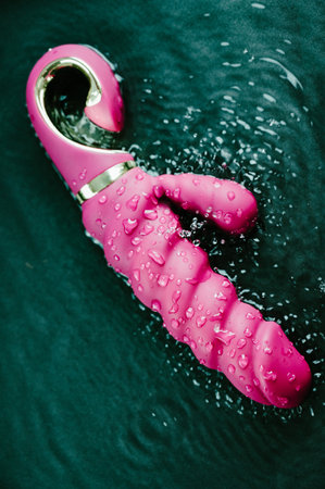 Pink ribbed vibrator in water. Circles on water around toyの写真素材