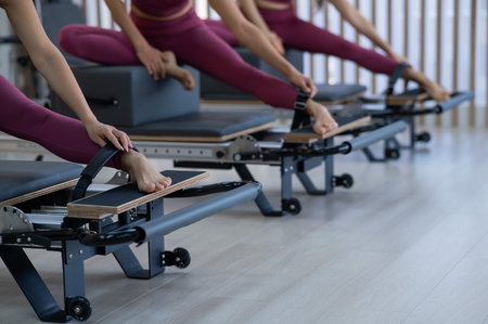 Three Asian women in pink sportswear doing pilates exercises with a reformer bedの写真素材
