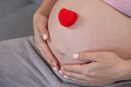 Caucasian pregnant woman holding heart on belly background. Third trimesterの写真素材