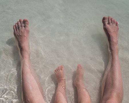 Top view of the legs of a one year old boy and his mother on the seashoreの写真素材