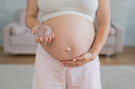Close up of pregnant womans belly holding glass globe