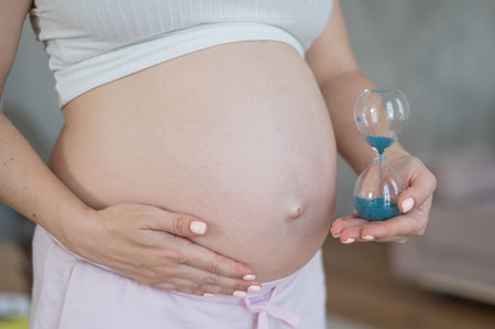 Close up of pregnant womans belly holding hourglass
