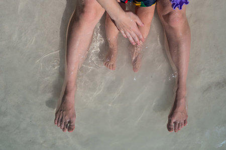 Top view of the legs of a one year old boy and his mother on the seashoreの写真素材
