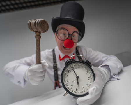 An elderly man dressed as a clown smashes an alarm clock with a hammerの写真素材