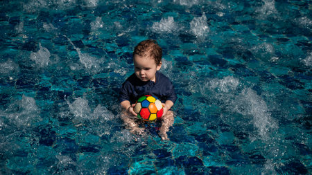 Caucasian one year old boy playing ball in swimming poolの写真素材