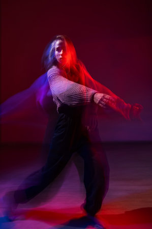 A young woman dances contemporary dances in blue and red light. Long exposure. Vertical photo