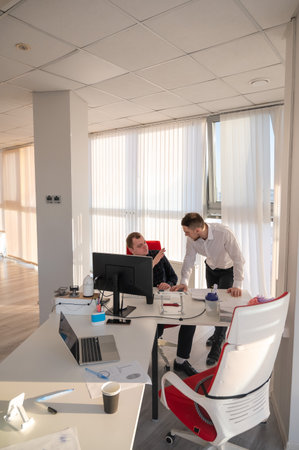 Caucasian man standing at colleagues desk discussing workの写真素材