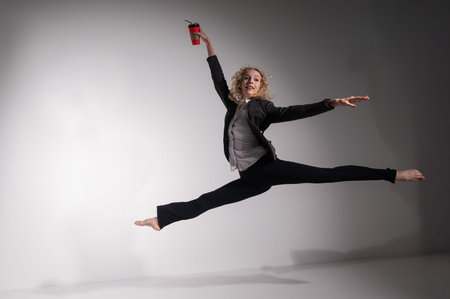 Barefoot ballerina in business suit jumping with a cup of coffee on a white background