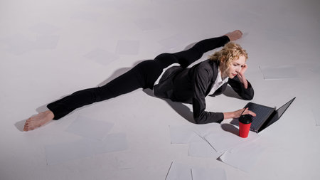 A ballerina dressed in a business suit sits in a middle twine, works at a laptop and drinks coffee....