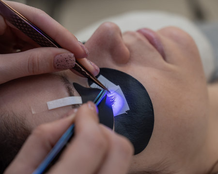 A woman undergoing eyelash extension procedure using an ultraviolet lamp