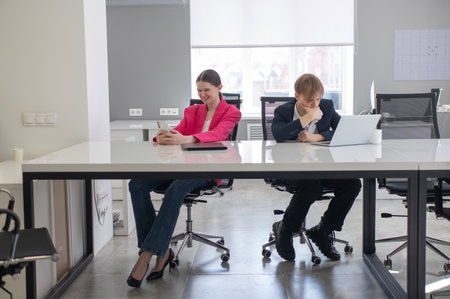 Caucasian Businesswoman Uses Smartphone While Colleague Has Problems At Workの写真素材