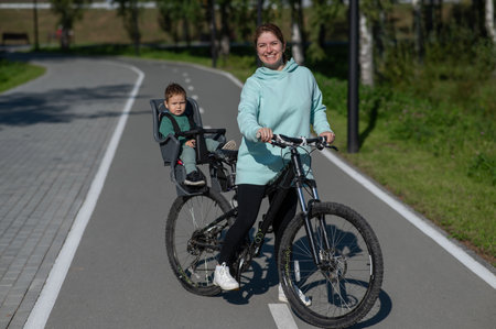 Caucasian woman riding a bicycle with her toddler son sitting behind her in a child seatの写真素材