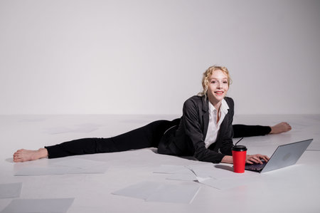 A ballerina dressed in a business suit sits in a middle twine, works at a laptop. Flexible woman...