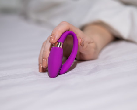 Woman holding curved purple vibrator while lying in bedの写真素材