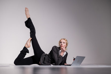 A ballerina dressed in a business suit poses for a laptop and drinks coffee. Flexible woman works at the computer.の写真素材