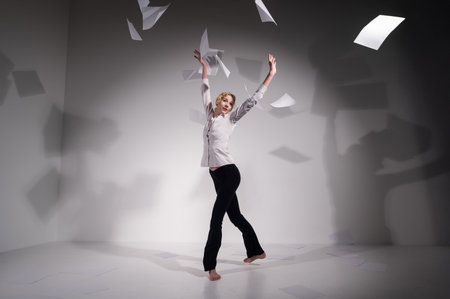 A graceful ballerina in a business suit throws documents. Business woman dance barefoot on a white background.の写真素材