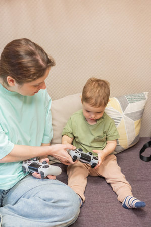 Caucasian woman teaches her little son to play console. Joystick in hands