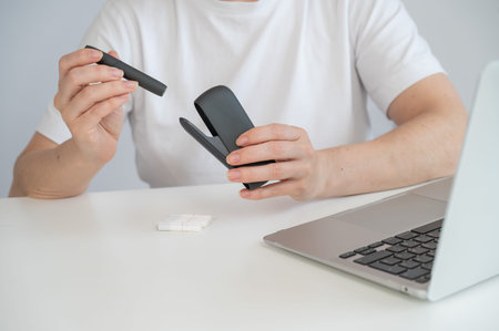 A woman smokes an electronic cigarette while working on a laptop. Tobacco heating system