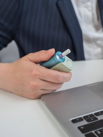 Business woman smoking an electronic cigarette while working on a laptop. Tobacco heating system
