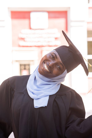 Portrait of happy african woman wearing hijab and graduation gownの写真素材