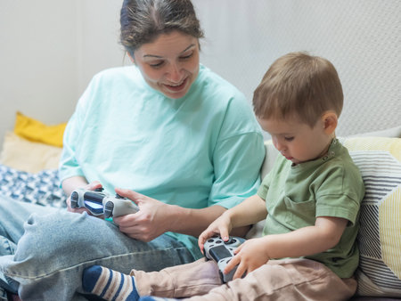 Caucasian woman teaches her little son to play console. Joystick in hands