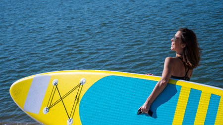 Caucasian woman walks along the beach and carries a sup board on the river in the city. Summer sport