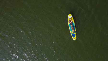 Caucasian woman riding a SUP board on the lake. View from above. Summer sport